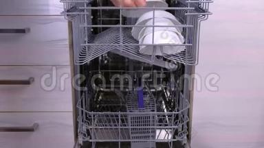 男人`手在洗碗机篮子里放了一个白色的脏盘子和餐具。